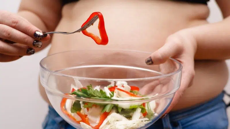 Egy tál salátát tartó túlsúlyos nő, mely állapot a lassú anyagcsere egyik tünete